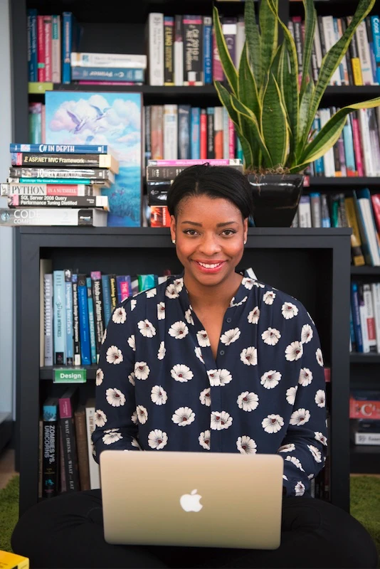 Women of Color working on a laptop looking at the camera smiling